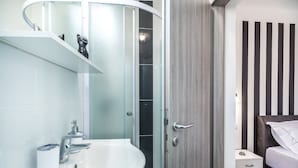 A modern bathroom with a white sink, a glass shower enclosure, and a wooden door. - Apartments & Rooms Sunshine Home - Double Room with balcony ( Black ) (Vela Luka)