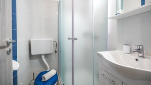 Une salle de bain avec un lavabo blanc, des toilettes bleues et une douche à parois de verre.