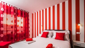 A hotel room with a striped red and white wall, a bed with red and white bedding, and a red curtain with polka dots.
