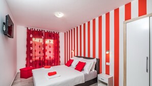 A modern bedroom with a bed, red curtains, a red and white striped wall, a small bedside table, and a wardrobe.