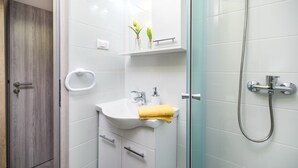 A modern bathroom with a glass shower enclosure, a white sink with a yellow towel, and a wooden door.