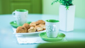 A table with a plate of pastries, a green cup, and a white vase with a plant.