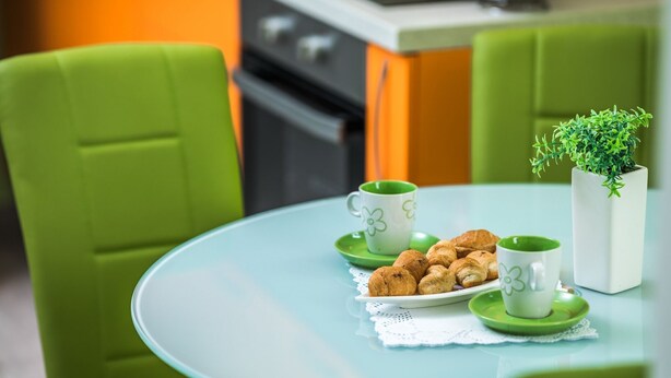 A table with a plate of croissants, two green cups with floral designs, and a small potted plant.