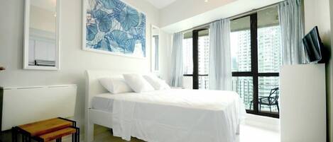 A modern bedroom with a large bed, a TV, and a view of a cityscape through large windows.