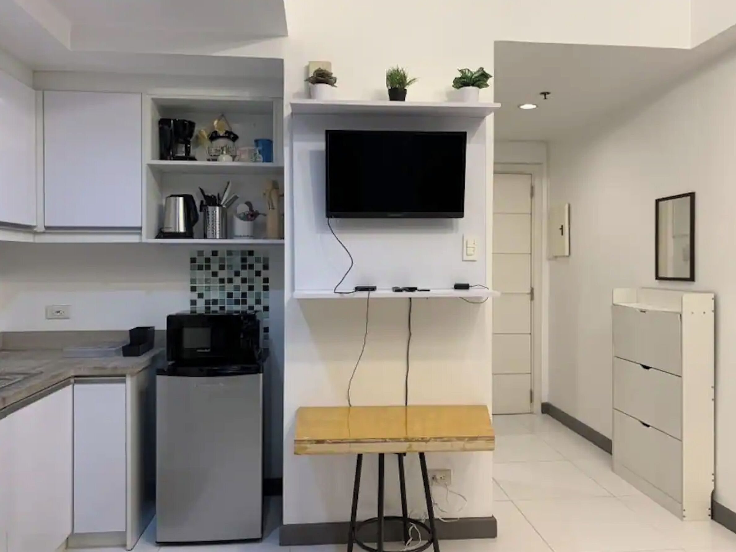 Ett modernt kök med vita skåp, en inbyggd mikrovågsugn, ett litet kylskåp, en träbänk och en platt-TV som är monterad på väggen.