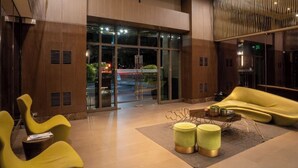 Un hall d’entrée moderne avec une entrée en verre, des sièges jaunes et une table basse centrale.