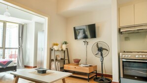 Un salon moderne doté d’un téléviseur à écran plat, d’un ventilateur sur pied, d’une table en bois et d’un coin cuisine avec un four.