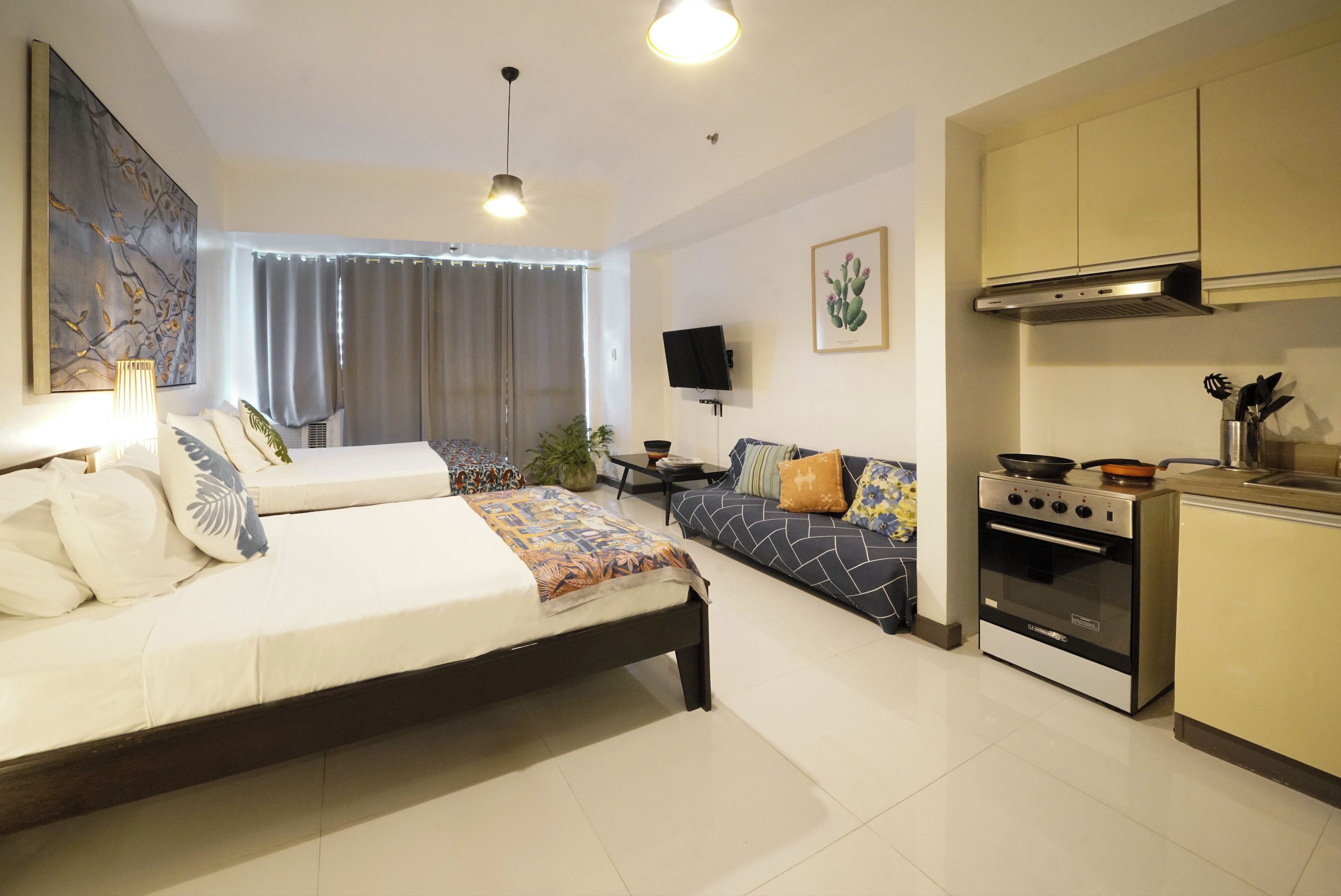 A modern bedroom with a bed, a sofa, a TV, and a kitchen area with a stove.