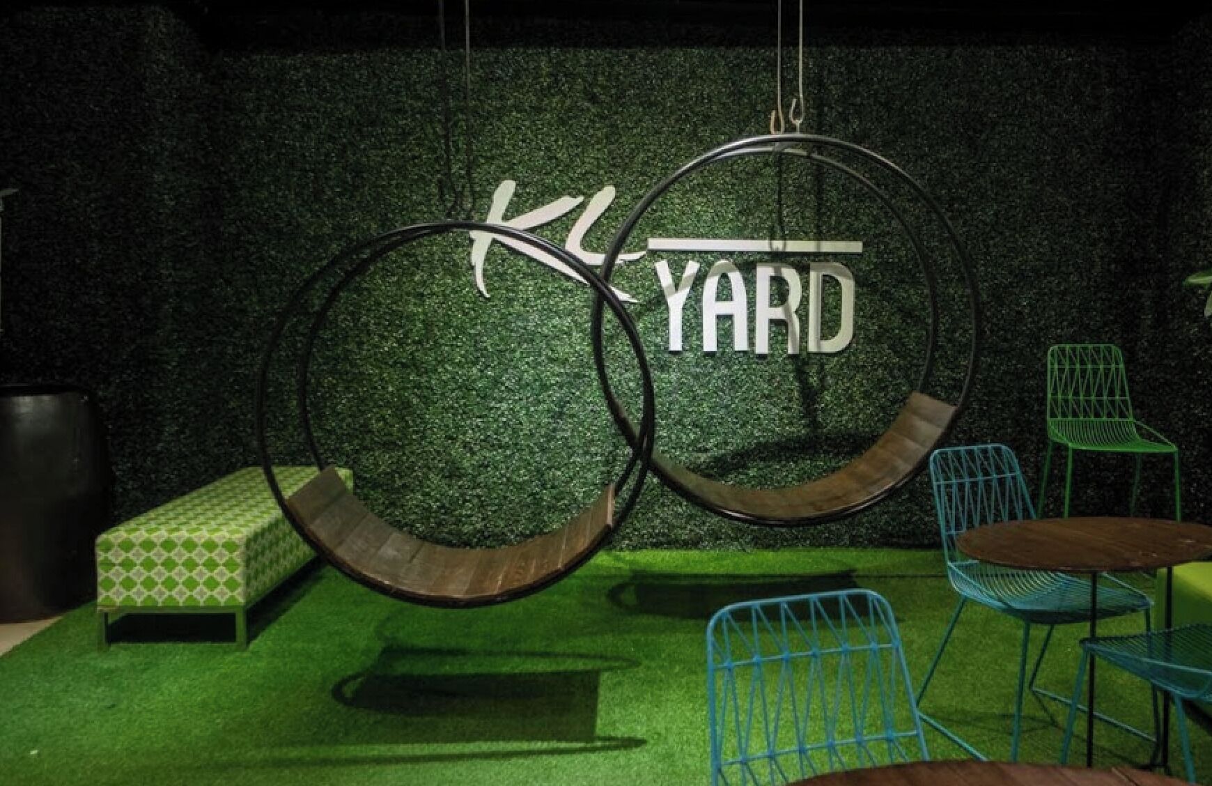 A hanging bicycle wheel structure with a sign that reads "YARD" against a green wall.