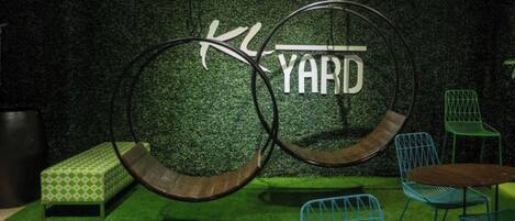 A hanging bicycle wheel structure with a sign that reads "YARD" against a green wall.