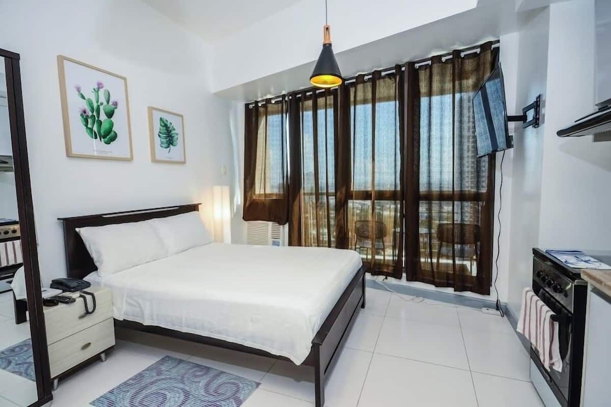 A bedroom with a bed, bedside table, lamp, and a window with curtains.