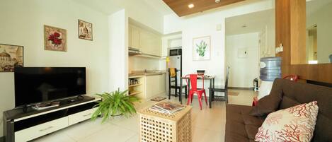A living room with a TV, a sofa, a red chair, a coffee table, and a kitchen in the background.
