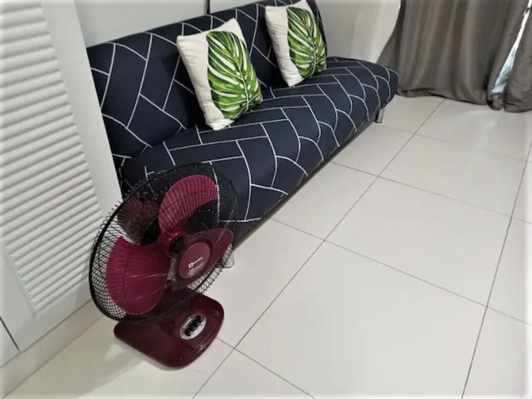 Een kamer met een witte radiator, een donkerblauwe bank met een geometrisch patroon en een rode ventilator.