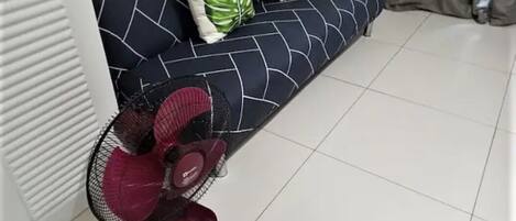 Een kamer met een witte radiator, een donkerblauwe bank met een geometrisch patroon en een rode ventilator.