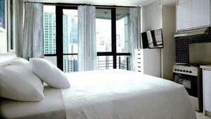 Une chambre d’hôtel avec un grand lit, une télévision, une kitchenette et une vue sur le paysage urbain par la fenêtre.