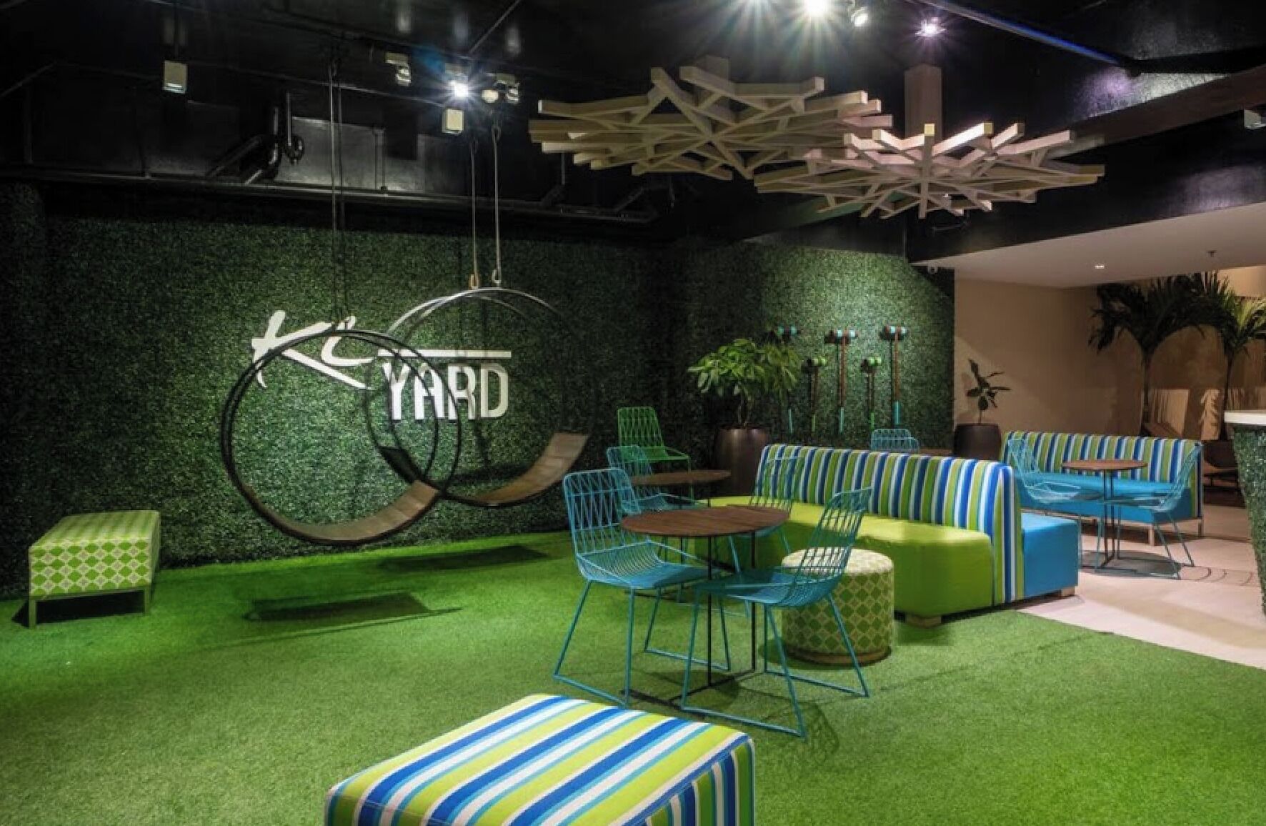 A modern lounge area with green artificial grass, striped seating, and a large 'YARD' sign.