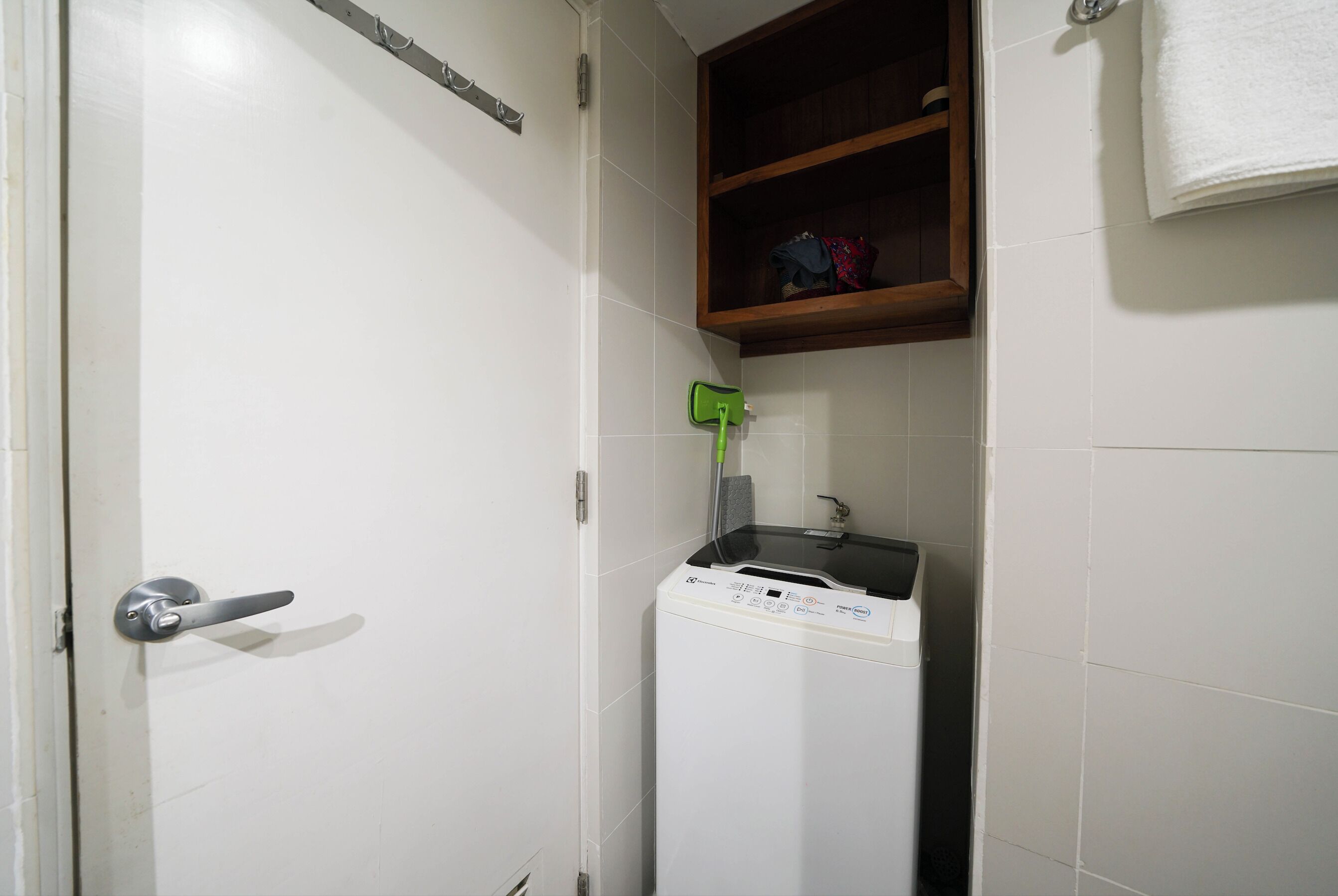 A laundry room with a washing machine, a shelf with towels, and a door with a handle.