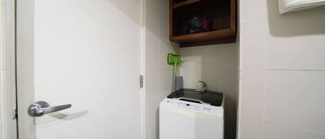 A laundry room with a washing machine, a shelf with towels, and a door with a handle.