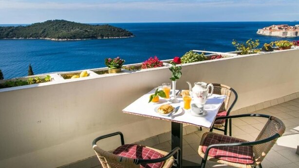 A terrace with a table set for breakfast, overlooking a coastal view with a distant island and a fortified structure.