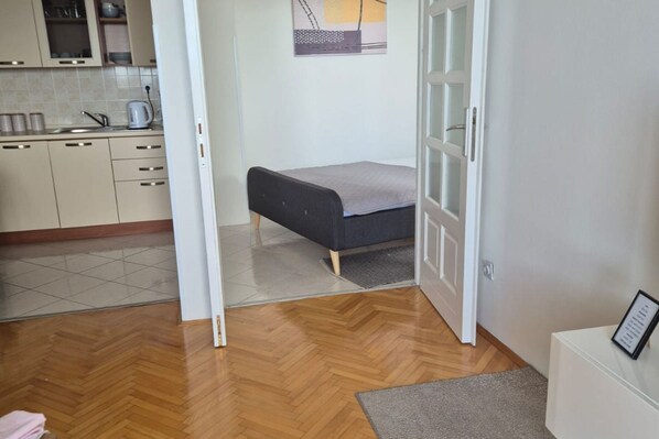 Una habitación pequeña con cama, kitchenette y puerta que da a otra estancia.