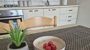 A kitchen with a stove, oven, and a sink. There is a table with a bowl of fruit and a potted plant.