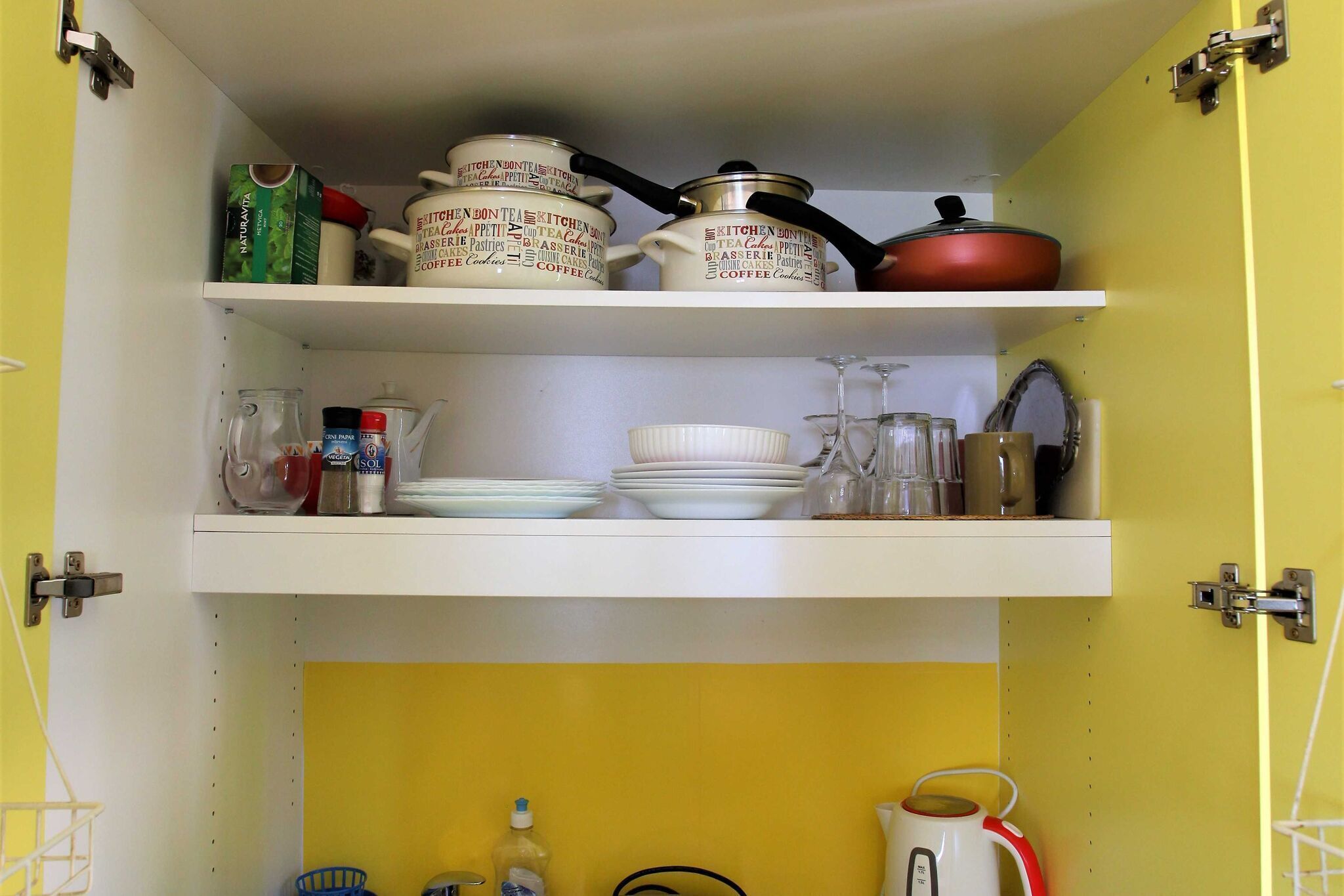 Una cocina con dos estantes blancos: uno con utensilios de cocina y otro con platos y tazas.