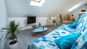 A modern living room with a blue and white patterned sofa, a glass coffee table, a potted plant, a flat-screen TV, and a skylight. - Apartments & Rooms Sunshine Home - Studio Apartment (Vela Luka)