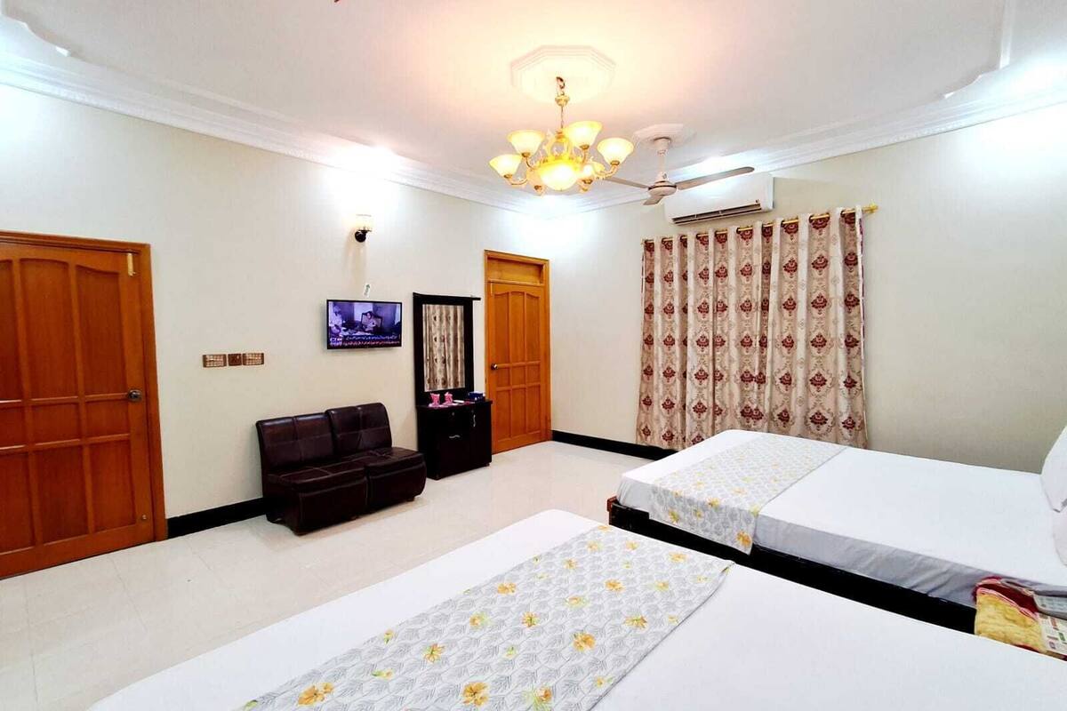 A hotel room with two beds, a TV, a ceiling fan, and a chandelier.