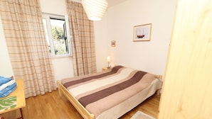 A bedroom with a wooden bed, a window with curtains, a bedside table with a lamp, and a framed picture on the wall.