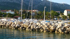 A marina with boats, a rocky breakwater, and houses in the background.