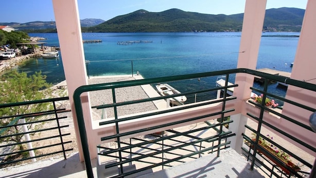 A balcony with a view of a calm sea, a dock, and a mountainous landscape in the background. - Apartments Ereš Zuronja-One-Bedroom Apartment with Sea View 2 (Putnikovici)
