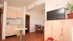 A compact kitchen with wooden cabinets, a dining table, and a TV on a stand. - Apartments Ereš Zuronja-One-Bedroom Apartment with Sea View 2 (Putnikovici)