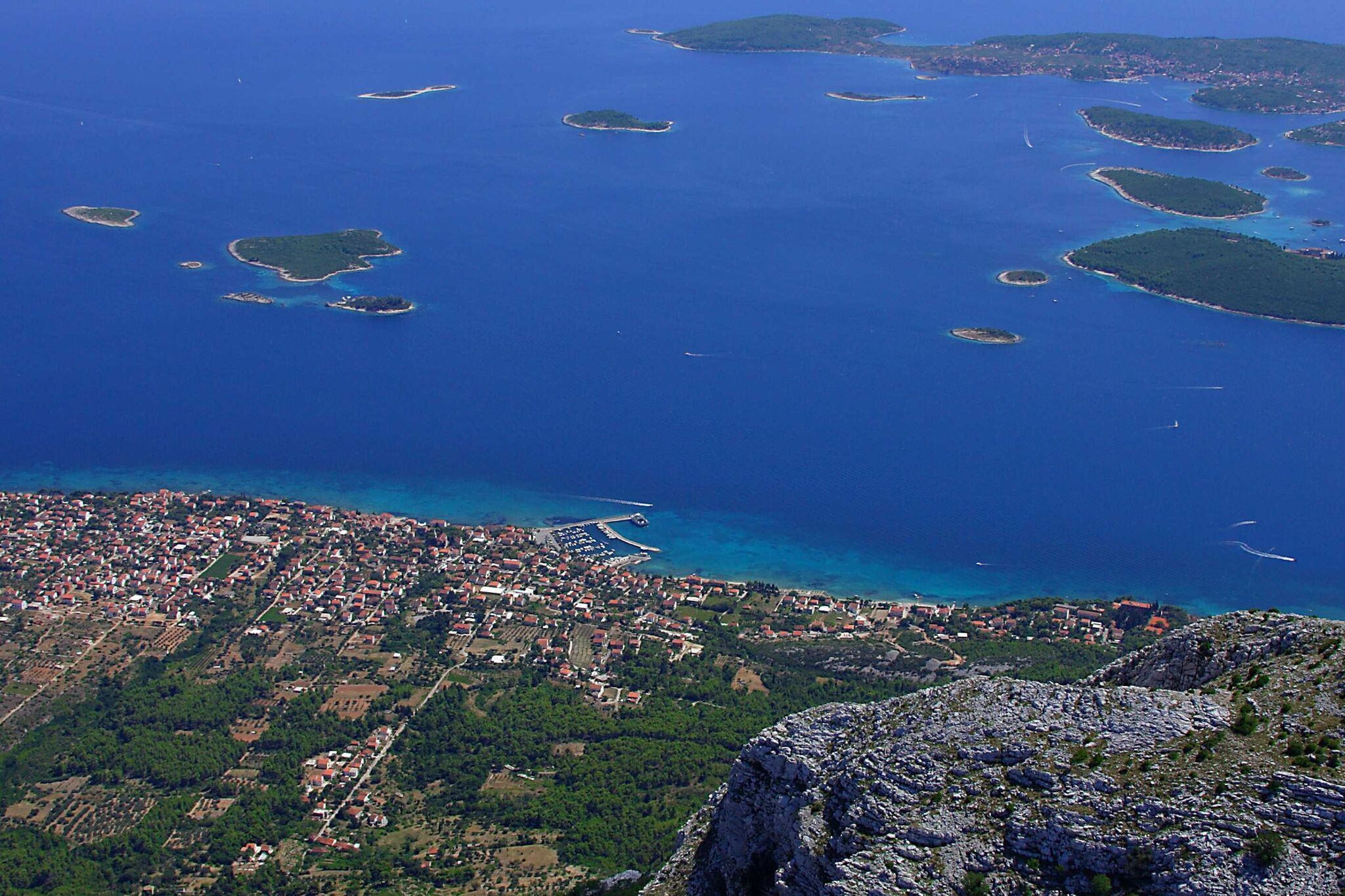 An aerial view of a coastal town with a rocky coastline, numerous small islands, and a densely built urban area with visible streets and buildings.