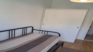 A single bed with a metal frame, a white door in the background, and a wooden floor.