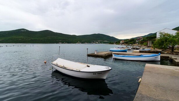 Un lago tranquilo con barcos amarrados en un muelle, rodeado de colinas y un pueblo pequeño al fondo.