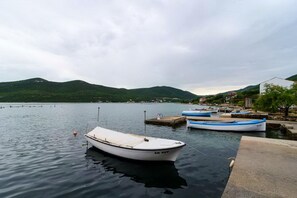 A calm lake with boats docked at a pier, surrounded by hills and a small town in the background. - Apartments Ereš Zuronja-One-Bedroom Apartment with Sea View 3 (Putnikovici)