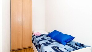 Un dormitorio pequeño con una cama individual, un armario de madera y una pared blanca lisa.