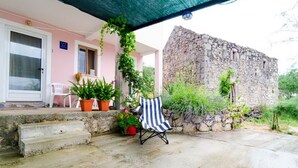Un edificio de piedra con fachada rosa, un patio cubierto con escalones, una silla a rayas y plantas en macetas.