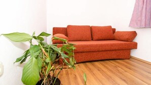 Una habitación con un sofá rojo, una planta grande de color verde y un suelo de madera.
