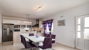 A modern kitchen with white cabinets, stainless steel appliances, and a dining area with a white table and purple chairs.