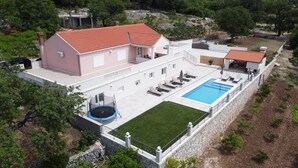 A two-story house with a swimming pool, a tennis court, and a fenced garden area.