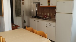 A compact kitchen with a gas stove, sink, and white cabinets. There is a dining table with chairs and a TV mounted on the wall.