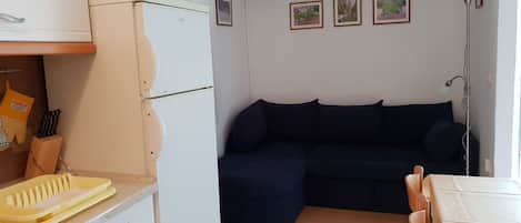 A compact living space with a kitchenette, a dark blue sofa, and a dining area.