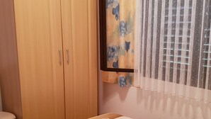 A bedroom with a wooden wardrobe, a bed with a striped bedspread, and a window with a floral curtain.