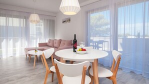 Ein modernes Wohnzimmer mit einer Couch, einem Esstisch mit Stühlen, einer Weinflasche und Obst.