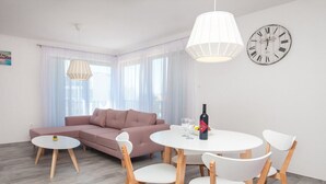 Ett modernt vardagsrum med en soffa, ett matbord med stolar, en klocka på väggen och en hänglampa.