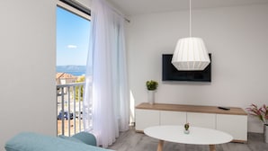 A modern living room with a sofa, a round table, a TV mounted on the wall, and a balcony with a view of the sea. - Apartments Dva Galeba - One Bedroom Apartment with Sea View (105) (Bol)