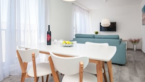 A modern living room with a dining table, chairs, a sofa, and a TV mounted on the wall. - Apartments Dva Galeba - One Bedroom Apartment with Sea View (105) (Bol)