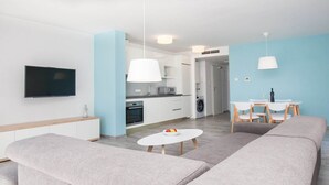Una sala de estar moderna con un sofá gris, una mesa de centro blanca y un comedor con una mesa blanca y sillas de madera.