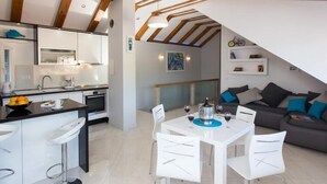A modern kitchen with white cabinets, a black countertop, and a dining area with white chairs and a table. - Mali Skoj Apartment - Two-Bedroom Apartment with Sea View (Sudurad)
